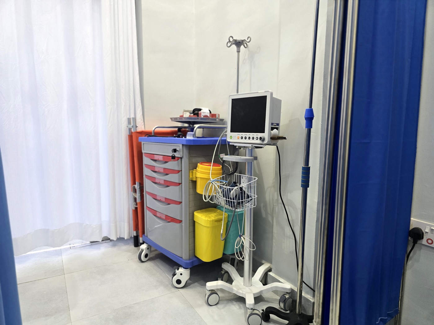 An emergency trolley and patient monitor beside a stretcher at MacWish Medical Centre