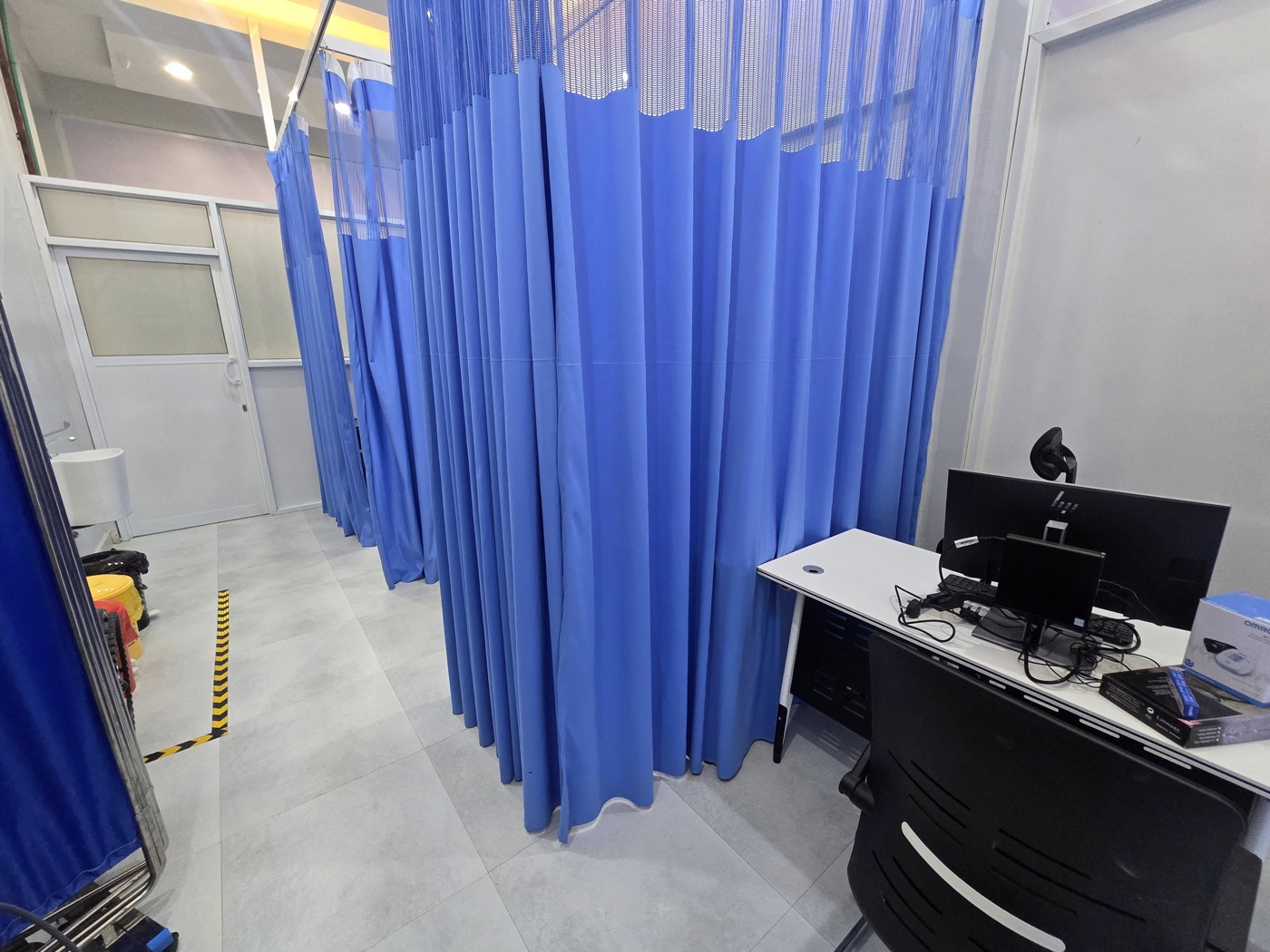 A consulting desk beside curtained examination bays at MacWish Medical Centre
