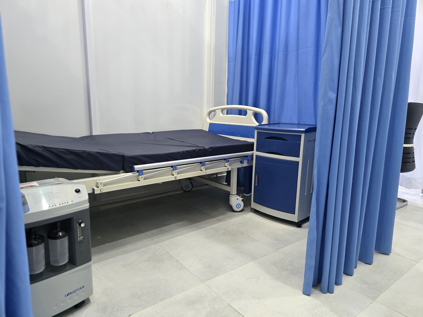 A curtained bed with its bedside cabinet at MacWish Medical Centre
